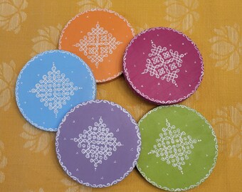 May include: Five round coasters with different colored backgrounds and white geometric designs. The coasters are made of wood and have a smooth finish.