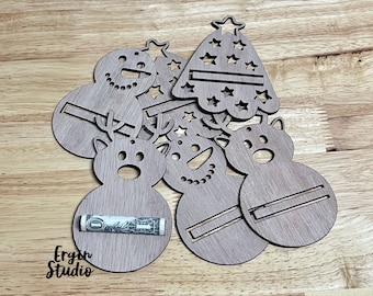 May include: Wooden Christmas-themed gift card holders in the shape of snowmen, reindeer, and a Christmas tree. One holder has a rolled-up dollar bill. The holders are made of light brown wood and have cut-out details.
