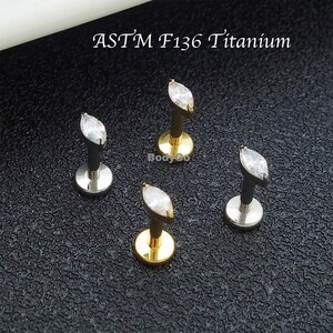 May include: Four pieces of body jewellery. Each piece features a marquise-cut, clear gemstone. Two pieces have a gold-coloured base, and two have a silver-coloured base. The text "ASTM F136 Titanium" is printed in the image.