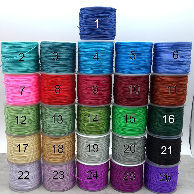 May include: A selection of coloured cord spools, numbered 1 to 26. The spools display a spectrum of hues, including blue, green, pink, red, and purple. The arrangement highlights the variety of colours available for crafts or jewellery projects.