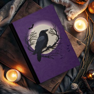 Puede incluir: Un diario morado con un cuervo negro posado en una rama frente a una luna llena. El cuervo está silueteado contra la luna, y hay murciélagos volando en el fondo.