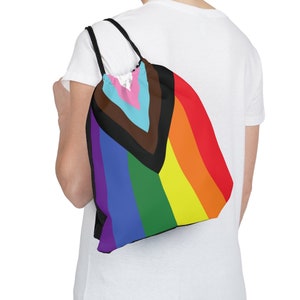 May include: A rainbow drawstring bag with a black triangle in the center. The triangle is filled with pink, light blue, and brown stripes. The bag is made of a lightweight fabric and has a drawstring closure.