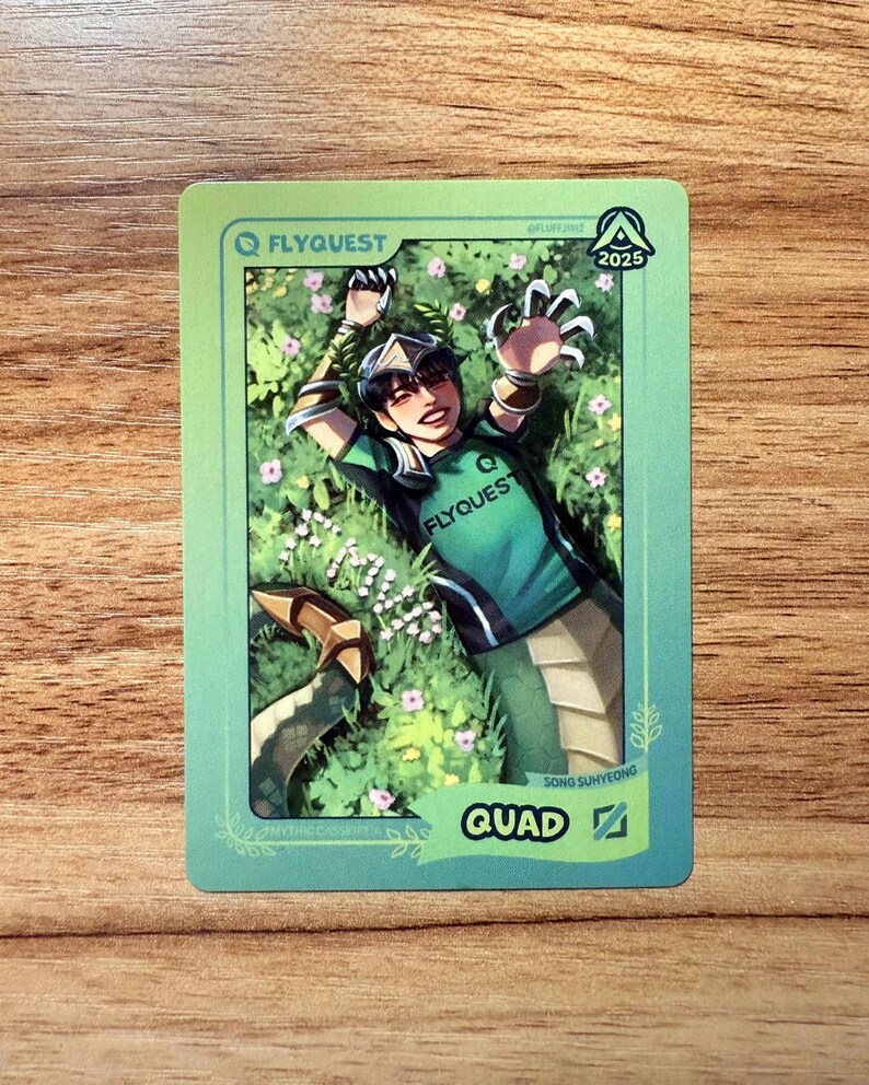 A trading card featuring lolesports LCS and LCK professional player Song Suhyeong, aka Quad, in the FlyQuest 2025 green jersey. He is drawn laying on grass with a smile, extending an arm upward as his signature League of Legends champion, Mythic Cassiopeia, so he has a snake tail. The card has a green gradient border with the text "QUAD" and the Mid Lane icon at the bottom right, 'MYTHIC CASSIOPEIA' bottom left, the LTA North logo and 2025 top right, and the FLYQUEST name and logo at top left.
