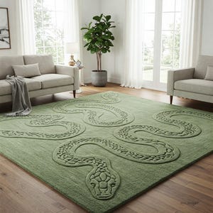 Peut inclure: Un tapis vert avec un motif de serpent. Le serpent est en relief et texturé, avec une tête et un corps détaillés. Le tapis rectangulaire est posé sur un parquet, avec un canapé et une chaise en arrière-plan.