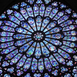 May include: A large, circular stained glass window with a blue, purple and red colour scheme. The window is divided into many small sections, each with a different design. The centre of the window features a smaller, circular design.