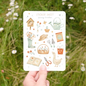 May include: A sticker sheet with a spring garden theme. The sheet features illustrations of gardening tools, flowers, a birdhouse, a watering can, and a goose. The text "STICKER SHEET spring garden" is at the top.