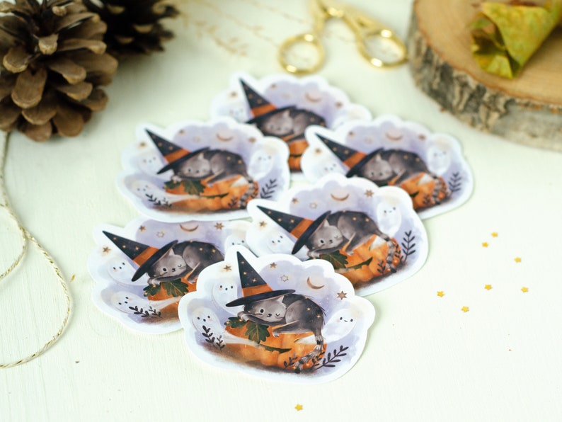 May include: A collection of Halloween-themed stickers featuring a gray cat wearing a witch hat, resting on a pumpkin. The stickers have a whimsical design with ghosts, moons, and stars, perfect for seasonal crafts.