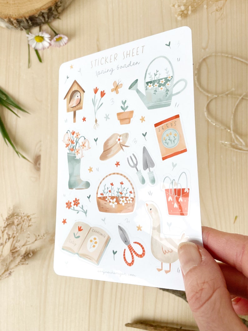 May include: A sticker sheet with a spring garden theme. The sheet features illustrations of gardening tools, flowers, a watering can, a birdhouse, and a goose. The text "STICKER SHEET Spring Garden" is at the top. The stickers are in soft pastel colours.