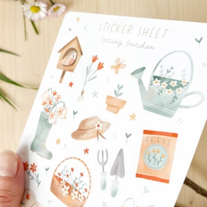 May include: A sticker sheet featuring watercolour illustrations of garden-themed items, including a birdhouse, flowers, a watering can, and gardening tools. The text "STICKER SHEET Spring Garden" is at the top.