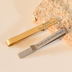 Peut inclure: Deux pinces à cravate gravées. Une pince à cravate dorée porte l'inscription "Bestman Groom & Jacob 3.20.2021". L'autre pince à cravate argentée porte l'inscription "Thank you for everything x".
