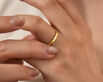 May include: A gold ring with the word "UTILA" engraved on the band. The ring is on a finger, and the image is a close-up shot. The ring is a simple band design, and the gold color is bright and shiny.