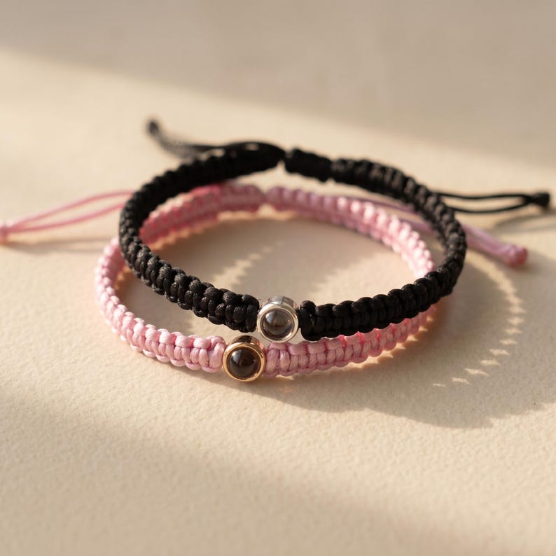 Peut inclure: Deux bracelets d'amiti&eacute; faits &agrave; la main. L'un est noir et tress&eacute;, l'autre rose et tiss&eacute;. Chaque bracelet comporte un petit charme rond. Les bracelets sont sur un fond neutre.