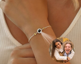 May include: A silver bracelet with a black and white photo charm. The charm is surrounded by small yellow stones. The bracelet is worn on a person's wrist.