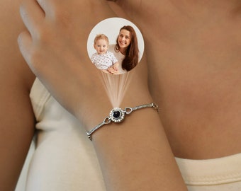 May include: A silver bracelet with a black stone in the center. The stone projects a photo of a woman and a child.