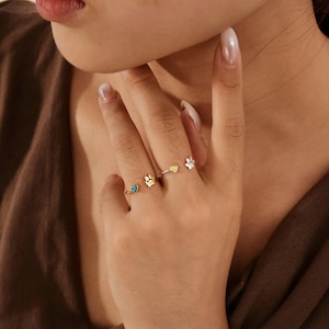 May include: A set of three adjustable rings featuring animal-themed designs. One gold-tone ring has a small blue heart, another gold-tone ring features a paw print, and a silver-tone ring displays a small paw print with a tiny heart accent.