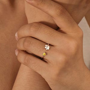 May include: A silver open-style ring featuring a small paw print charm on one end and a single yellow heart-shaped gemstone on the other. The band is thin and metallic, designed to wrap partially around the finger with an adjustable open gap.