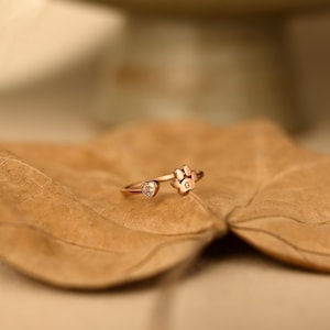 May include: A rose gold ring featuring an open band design with a small heart-shaped stone on one end and a paw print charm on the other. The paw print charm is engraved with the letter G, and the heart-shaped stone is clear and faceted.
