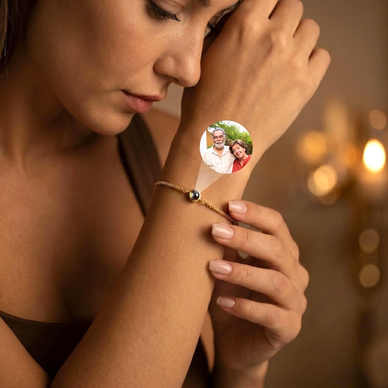 May include: A gold-toned chain bracelet featuring a central circular charm that projects a small, circular color photograph of an older man with a beard and a woman standing together. The bracelet has a delicate, thin link design.