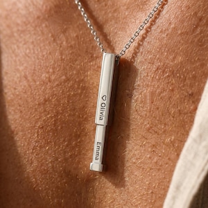 Op de afbeelding: Een zilverkleurige ketting met een verticale hanger. De hanger is gegraveerd met de namen "Olivia" en "Emma". De ketting heeft een fijne schakelketting. De hanger is rechthoekig met afgeronde randen.