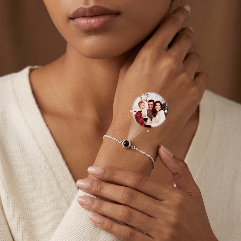 May include: A silver-toned chain bracelet featuring a central circular pendant. The pendant projects a circular image of a family consisting of two adults and a child, with a star-shaped decoration visible in the background of the projected scene.