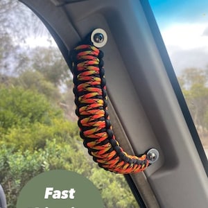 Puede incluir: Una manija de paracord negra, amarilla y naranja está unida al interior de un vehículo. La manija está asegurada con dos tornillos plateados. La manija es una característica de seguridad para los pasajeros.