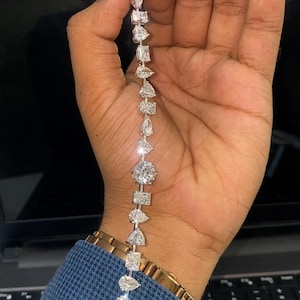 Puede incluir: Un deslumbrante brazalete de diamantes con una variedad de formas, incluyendo cortes redondos, pera y rectangulares. El brazalete se muestra sobre un fondo oscuro, resaltando el brillo de las gemas. Una lujosa pieza de joyería.