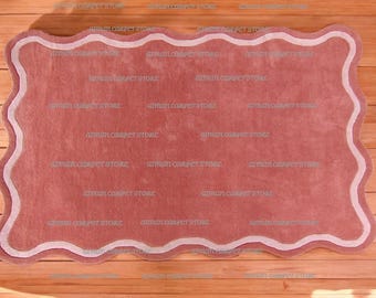 Puede incluir: Una alfombra rosa con un borde blanco festoneado. La alfombra está hecha de un material suave y mullido y tiene un brillo sutil.