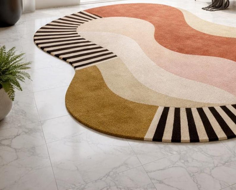 May include: A large, abstract area rug with a wavy design. The rug features a combination of colors, including brown, tan, pink, and gold. The edge of the rug has a striped pattern in black and tan.