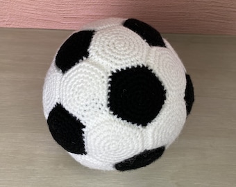 May include: A white and black crocheted soccer ball. The ball is made of yarn and has a textured surface.