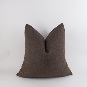 May include: A brown cushion with a textured fabric. The cushion is a solid colour and has a square shape. The cushion is on a white background.