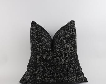 May include: A square decorative pillow with a textured black and gray pattern. The pillow has a soft, plush appearance and is designed for home decor. The fabric has a woven look, adding visual interest to the design.