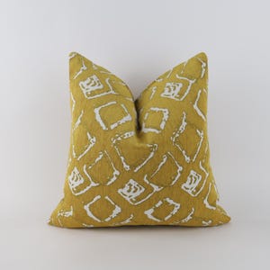 Könnte beinhalten: Senfgelbes Zierkissen mit weißem geometrischem Muster. Das quadratische Kissen besteht aus strukturiertem Stoff. Das Design zeigt ein sich wiederholendes Muster aus weißen Formen auf einem einfarbigen gelben Hintergrund.