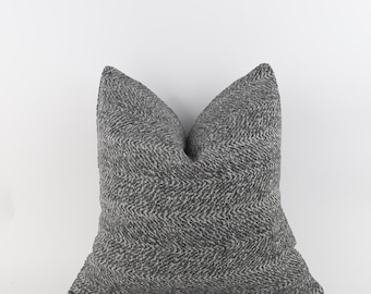 May include: A square decorative pillow with a gray and white herringbone pattern. The pillow has a soft, textured appearance and is designed for home decor. The pillow is against a white background.
