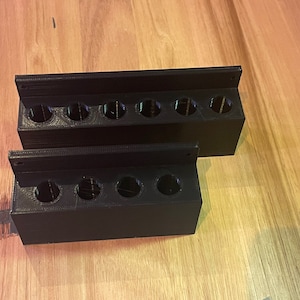Könnte beinhalten: Zwei schwarze Plastik-Organizer mit mehreren runden Löchern zum Verstauen von Kleinteilen. Die Organizer sind übereinander gestapelt.
