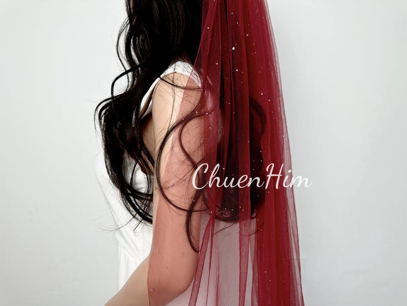 May include: A burgundy tulle veil with a sparkly finish. The veil is worn by a person with long dark hair.