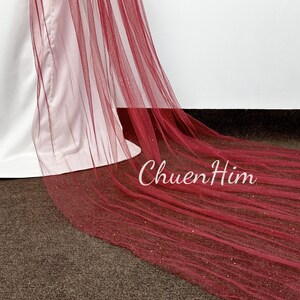 May include: A long, burgundy tulle veil with a sparkly finish. The veil is draped over a white dress.