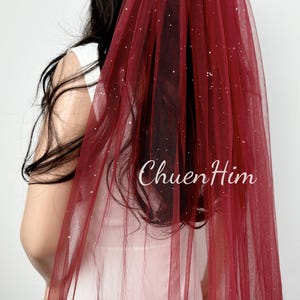 May include: A burgundy tulle wedding veil with silver glitter. The veil is sheer and has a delicate sparkle.