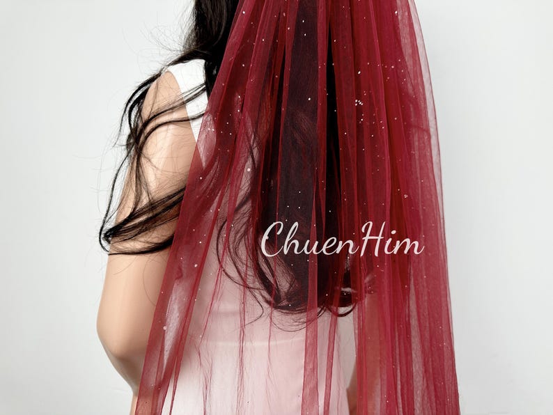 May include: A burgundy tulle wedding veil with silver glitter. The veil is sheer and has a delicate sparkle.
