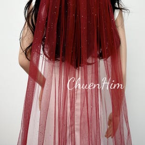 May include: A burgundy tulle veil with a sparkly finish. The veil is long and flowing, and it would be perfect for a wedding or other special occasion.