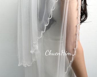 May include: A white bridal veil with a beaded edge. The veil is made of soft tulle and has a scalloped edge.