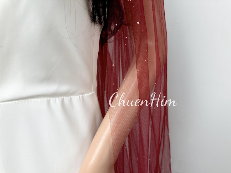 May include: A burgundy tulle shawl with silver glitter accents. The shawl is draped over a person's arm and shoulder.