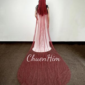 May include: A burgundy bridal veil with a sparkling finish. The veil is made of tulle and has a single layer. The veil is shown on a model wearing a white dress.