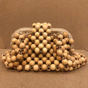 May include: A beige woven clutch bag made entirely of wooden beads. The beads are all the same size and shape, and they are arranged in a pattern that creates a textured surface.