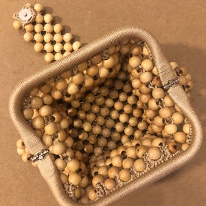May include: A square-shaped beaded bag made of natural wood beads. The bag has a clasp closure and a beaded strap.