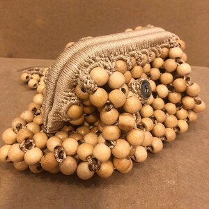 May include: A beige crocheted bag made of wooden beads. The bag has a zipper closure and a snap closure.