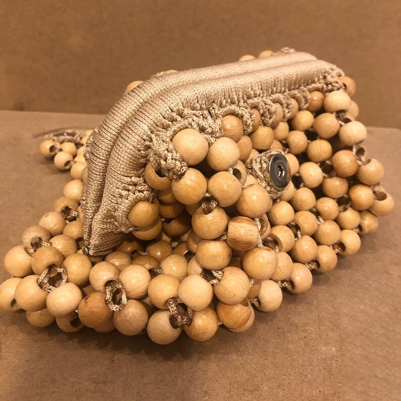 May include: A beige crocheted bag made of wooden beads. The bag has a zipper closure and a snap closure.