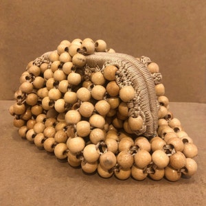 May include: A beige beaded bag made of wooden beads woven together. The bag has a zipper closure.