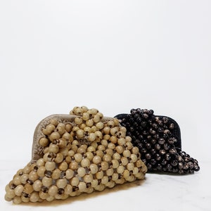 May include: Two beaded purses, one in natural wood tones and one in black. Both purses are made of small, round beads woven together.