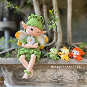 Könnte beinhalten: Eine handgefertigte Häkelfee-Puppe mit grünen und weißen Akzenten, einem Blumendetail und gelb-weißen Flügeln. Drei kleine gehäkelte Vögel in Grün, Gelb und Orange sitzen in der Nähe. Der Text "MeimyHandmadeVN" ist sichtbar.