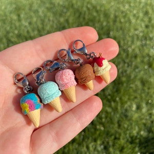 Op de afbeelding: Vijf miniatuur-ijsjes met zilveren karabijnhaken. De ijsjes zijn gemaakt van polymer clay en hebben verschillende kleuren en toppings, waaronder roze, blauw, bruin en rood.